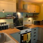Bumblebee Cottage kitchen with sage-green cabinets, wooden worktops, oven, hob, microwave and countryside splashback.